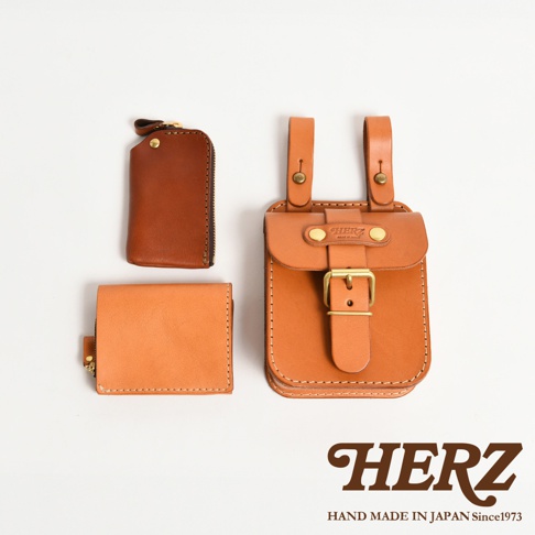 職人手作皮革經典腰袋，包含一個淺棕色拉鍊零錢包、一個橘棕色皮夾，以及一個較大的橘棕色皮質腰袋，腰袋有金屬釦環和皮帶固定。