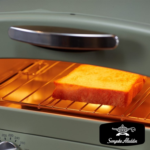 復古綠色多用途烤箱內，一片金黃色吐司放在金屬烤網上，烤箱內部加熱管散發溫暖光芒，上方是銀色金屬把手。
