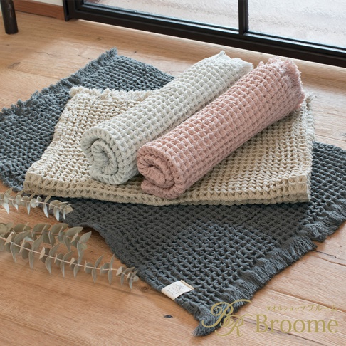 今治鬆餅加大浴墊，呈現蜂窩織紋，共有炭灰色、米白色、淺灰色、粉紅色四種顏色。其中兩款浴墊捲起，疊放在其他浴墊上，邊緣帶有流蘇。
