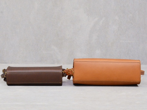 兩款職人手作皮革Organ極簡風拉鍊單肩包，一款為深棕色，另一款為原色皮革，皆為拉鍊開口設計，搭配可調節的皮革背帶。