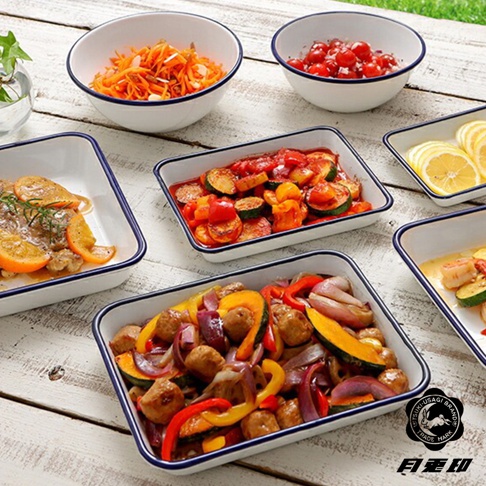 白色琺瑯調理盤，邊緣有深藍色滾邊。盤中盛有多種食材，包含雞肉佐柳橙片、燉煮番茄櫛瓜、烤蔬菜與肉丸，以及檸檬片。