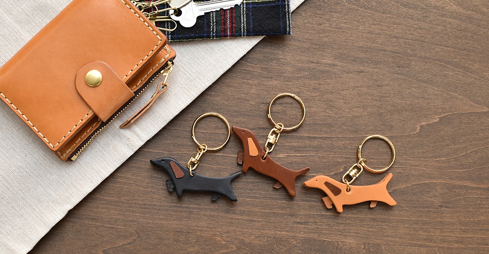 職人手作皮革狗狗造型鑰匙圈，共三款顏色：黑色、咖啡色、淺棕色。每個鑰匙圈皆以皮革製成，造型為臘腸狗，搭配金色金屬鑰匙環。