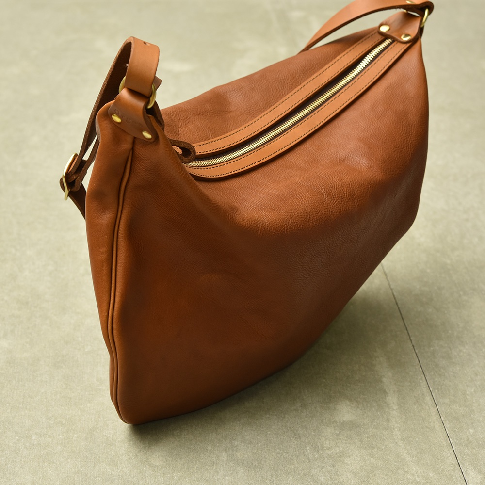 職人手作的咖啡色皮革Organ單肩半月包，包身呈現自然紋理，配有金色拉鍊和皮革提把。