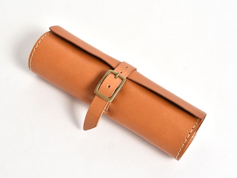 棕色皮革捲捲收納筆袋，附有黃銅扣環和皮帶，邊緣縫線明顯。