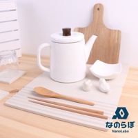 淺灰色珪藻土置物墊上擺放著白色帶咖啡色壺蓋的茶壺、木質湯匙、兩雙木筷、白色小鳥造型擺飾、白色小碗，以及一個木質砧板。