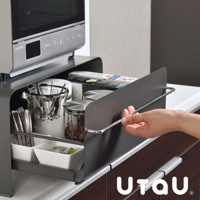 灰色金屬材質的抽屜式收納櫃，內有兩個白色小方碗，裝有茶包或咖啡包，以及透明玻璃罐裝有咖啡豆，上方置有咖啡濾網架，櫃體上方放置著微波爐。