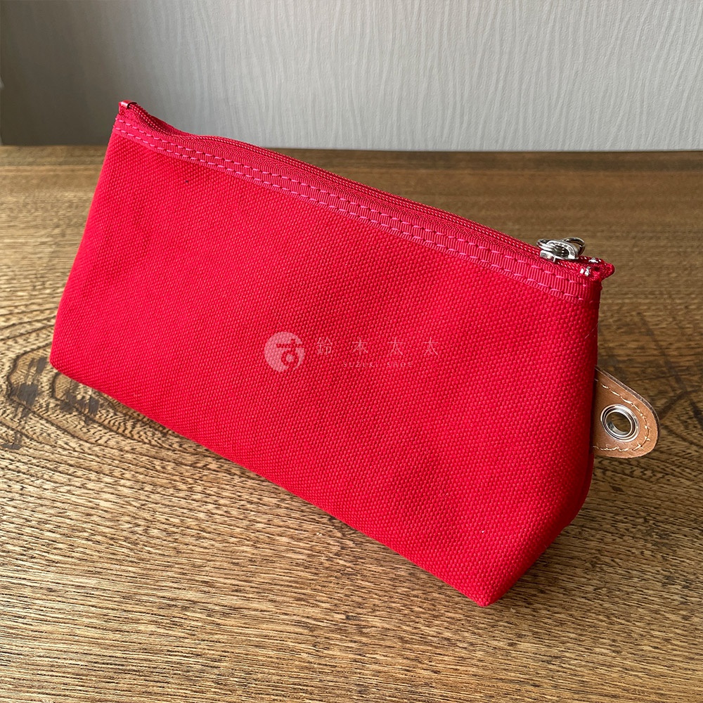 紅色石洗帆布製成的小型收納包，帶有拉鍊開口和一個皮革拉環，皮革拉環上附有金屬孔眼。