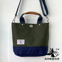 犬印純棉帆布兩用雙色托特包，主體為軍綠色帆布，底部拼接海軍藍色帆布，配有海軍藍色織帶提把和肩帶，以及棕色皮革提把。包身中央有金屬旋轉鎖扣，左側有一個印有品牌標誌的白色布標。