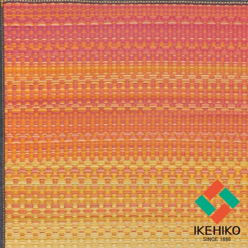 藺草編織瑜珈墊，漸層橘黃色調，帶有細緻的紋理，邊緣有黑色滾邊，右下角有品牌標誌。