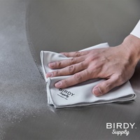 一手正用淺灰色超細纖維擦拭巾擦拭金屬表面，擦拭巾上有「BIRDY. Supply」品牌標誌。