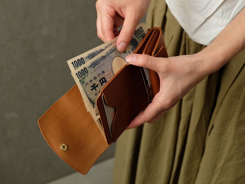 職人手作皮革Organ迷你短夾，採用棕色皮革製作，內有日圓鈔票及卡片，展現簡潔實用的設計。
