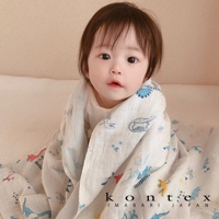 嬰兒被白色紗布毛巾包裹，上面印有藍色、粉紅色和黃色的恐龍圖案。