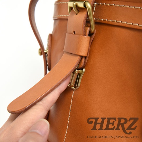 職人手作的棕色皮革後背包，特寫其皮質肩帶、黃銅扣環和縫線細節。