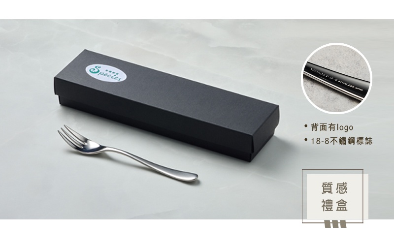 一個霧面不鏽鋼點心叉，置於黑色禮盒旁，叉子上印有品牌標誌。