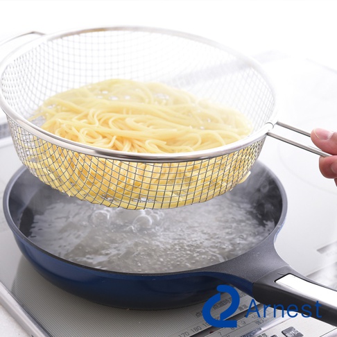銀色不鏽鋼手持濾網，網狀結構，盛裝著金黃色麵條，懸掛於藍色鍋子上方，鍋內有滾燙的沸水。