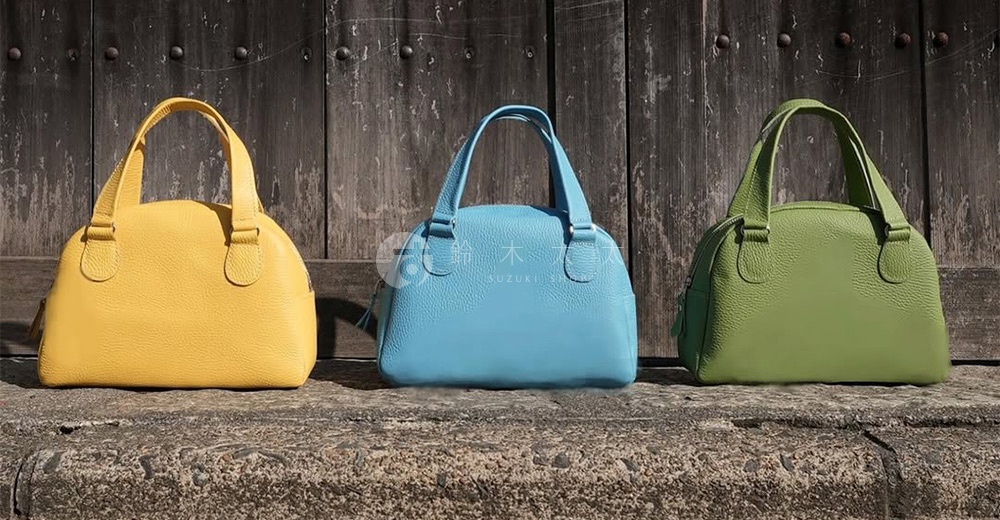 三款京都職人手作半月迷你手提包，分別為亮黃色、淺藍色與草綠色。包身呈現圓潤的半月形狀，搭配短提把，材質為觸感細膩的皮革，表面帶有細緻紋理。