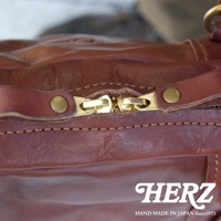 棕色皮革迷你波士頓包，特寫黃銅色拉鍊與皮革按鈕，展現職人手作的水洗加工質感。