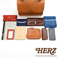 HERZ 品牌的手作皮革商品，包含錢包、筆記本、卡夾、手機及藍色印花頭巾。