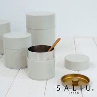 淺灰色簡約錫製茶葉罐，其中一個罐子內有一支木質勺子。周圍散落著兩個同款茶葉罐和一個金色內襯的淺灰色罐蓋。