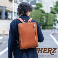 職人手作皮革商務電腦後背包，採用棕色皮革，方形簡約設計，側邊有拉鍊口袋，肩帶和提把皆為皮革材質。