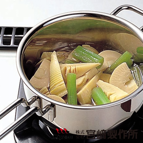 GEO無水料理萬能鍋，雙耳不鏽鋼醬汁鍋內盛滿切塊的竹筍與蔥段，正在烹煮中。鍋子置於爐架上，呈現銀色光澤。