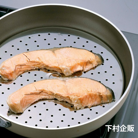 銀色金屬網狀蒸盤上放著兩塊烹煮過的鮭魚，蒸盤置於白色平底鍋內，鍋子旁有爐灶。