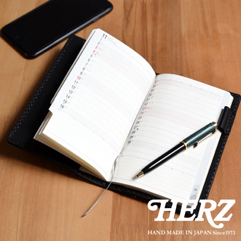 黑色皮革輕便記事本書套，內含一本白色紙張、帶有日期與時間格線的筆記本，一本綠色與金色的鋼筆置於書本中央。