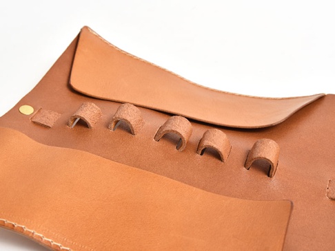 職人手作皮革捲捲收納筆袋，淺棕色天然皮革製成，袋面有五個皮革環，可固定筆類，另有金屬扣件。