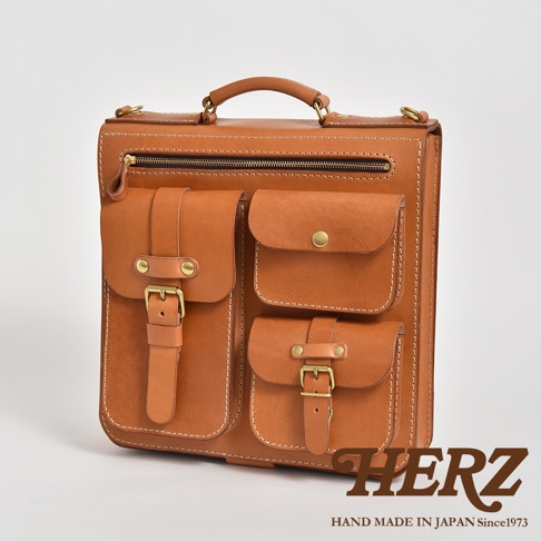 棕色皮革三口袋三用後背包，正面有兩個帶有銅扣和皮帶的貼袋，上方有一個拉鍊袋和一個提把，整體設計簡潔大方，材質為天然皮革。