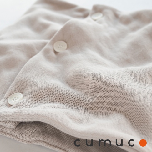 公大株式會社 CUMUCO 品牌標誌，搭配米白色嬰兒連身衣的近拍細節，顯示衣物的紋理與鈕扣。