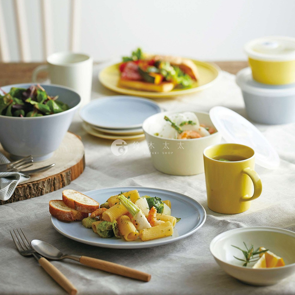 淺藍色美濃燒淺碗盛著沙拉，旁邊是另一個淺藍色盤子，上面放著義大利麵和麵包。右側有一個黃色馬克杯、一個淺黃色碗和兩個黃色儲物罐。