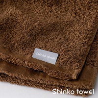 MAISON BLANC 輕奢柔膚匹馬棉浴巾，一條深棕色、觸感柔軟的毛巾，特寫顯示其細膩的織紋和邊緣的流蘇細節，標籤上印有「Shinko towel」。