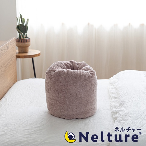 粉色絨毛材質的甜甜圈形狀枕頭，置於白色床單上，枕頭上方有抽繩束口的設計。