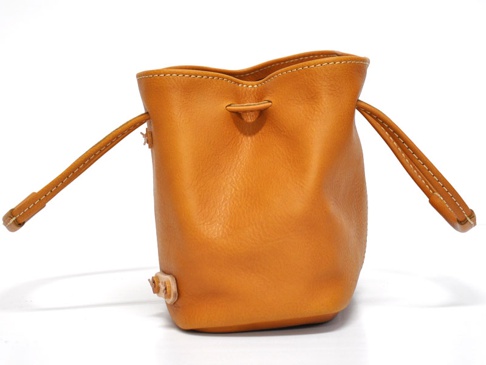 圓筒形橘棕色皮革束口兩用包，有兩條短提把，側邊有兩個可調整的固定點。