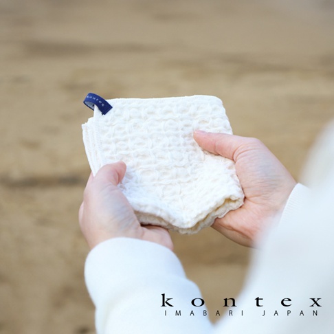 雙手捧著白色棉麻混紡方巾，方巾表面有鬆餅紋路，左上角有一個藍色品牌標籤。