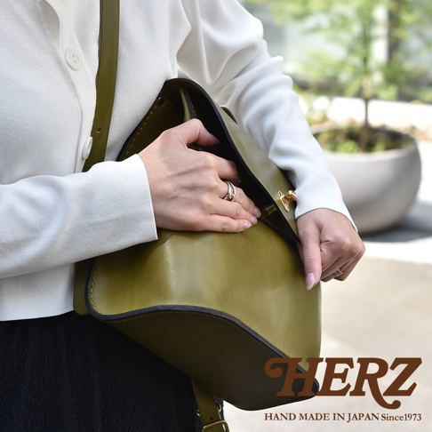 職人手作皮革翻蓋迷你後背包，橄欖綠色，皮革材質，設有金色鎖扣，由一位女性展示。