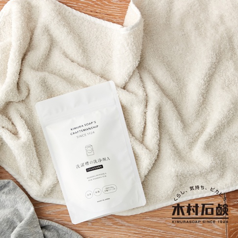 白色夾鏈袋裝的洗衣槽清潔粉，上面印有品牌名稱 KIMURA SOAP'S CRAFTSMANSHIP SINCE 1924。產品標示日文「洗槽槽的洗淨劑A」及英文「WASHING POWDER A FOR WASHING TUB」。產品置於淺米色毛巾上，背景為木紋桌面。