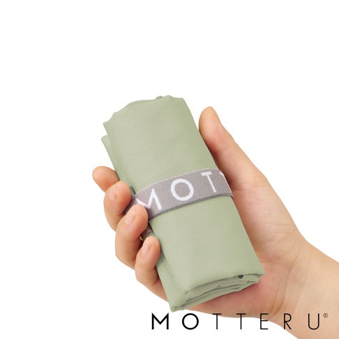 一隻手持著淺綠色、可摺疊的束口袋，袋身以灰色鬆緊帶束住，鬆緊帶印有白色「MOT」字樣。