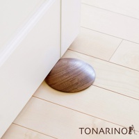 天然實木門擋，圓弧形狀，木紋清晰，深棕色澤，置於白色門板與淺色木地板之間，防止門撞擊牆壁。