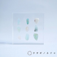 透明方形壓克力塊中，以九宮格方式陳列著九顆近似橢圓形的細石標本，顏色包含淺藍、淺綠、淡粉及白色，部分標本帶有天然紋理。