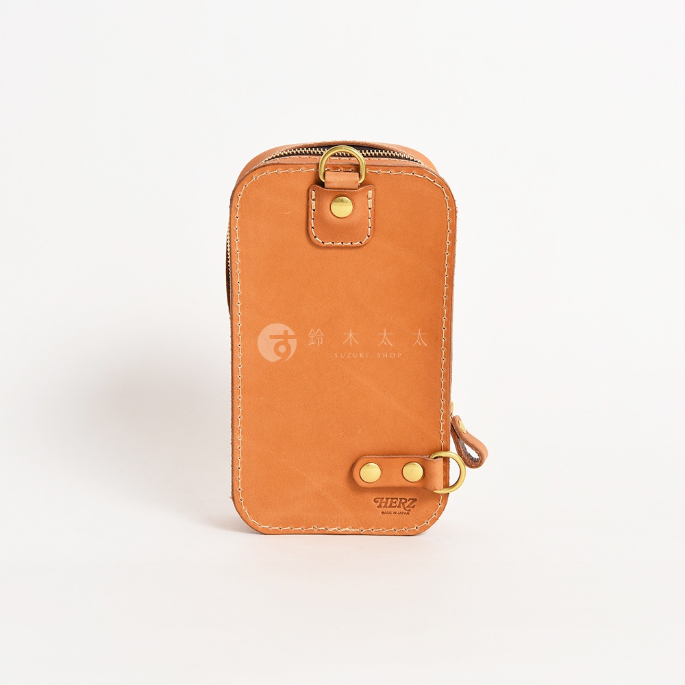 一個由日本HERZ品牌製作的棕色皮革斜背包，包包正面有燙金的日文標誌和英文標誌HERZ，包包上方和下方各有一個金屬扣環，包包右側有一個拉鍊，包包整體呈現簡約的風格。
