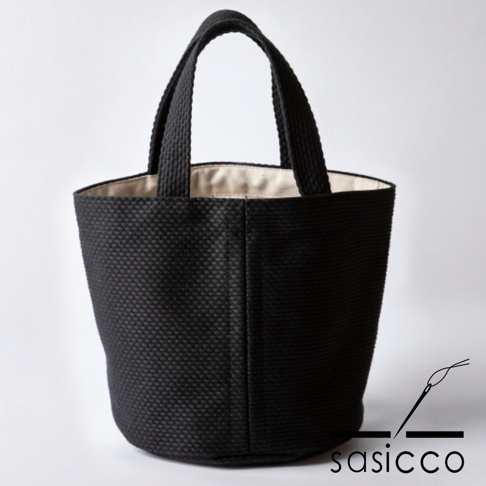 黑色三河木綿刺子織圓底水桶包，有兩個提把，包身呈現立體織紋，內裡為米白色。