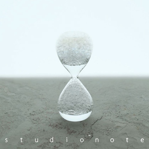 透明玻璃製成的迷你泡泡沙漏，中間有細長的連接處。上半部充滿細小的白色氣泡，下半部也聚集了許多氣泡，呈現流動感。產品放置在灰色紋理的表面上，背景為淺色。