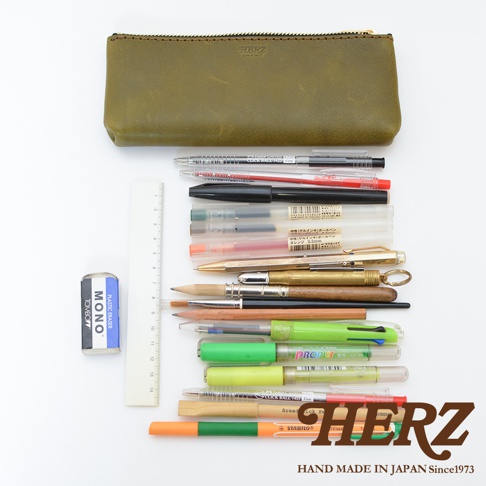 一只橄欖綠皮革筆袋，旁邊有橡皮擦、尺以及一疊各式各樣的筆，包含鋼筆、原子筆、螢光筆等。
