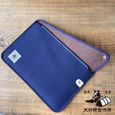深藍色純綿帆布平板收納包，內裡為棕色，設有磁扣，包上印有日文標誌。