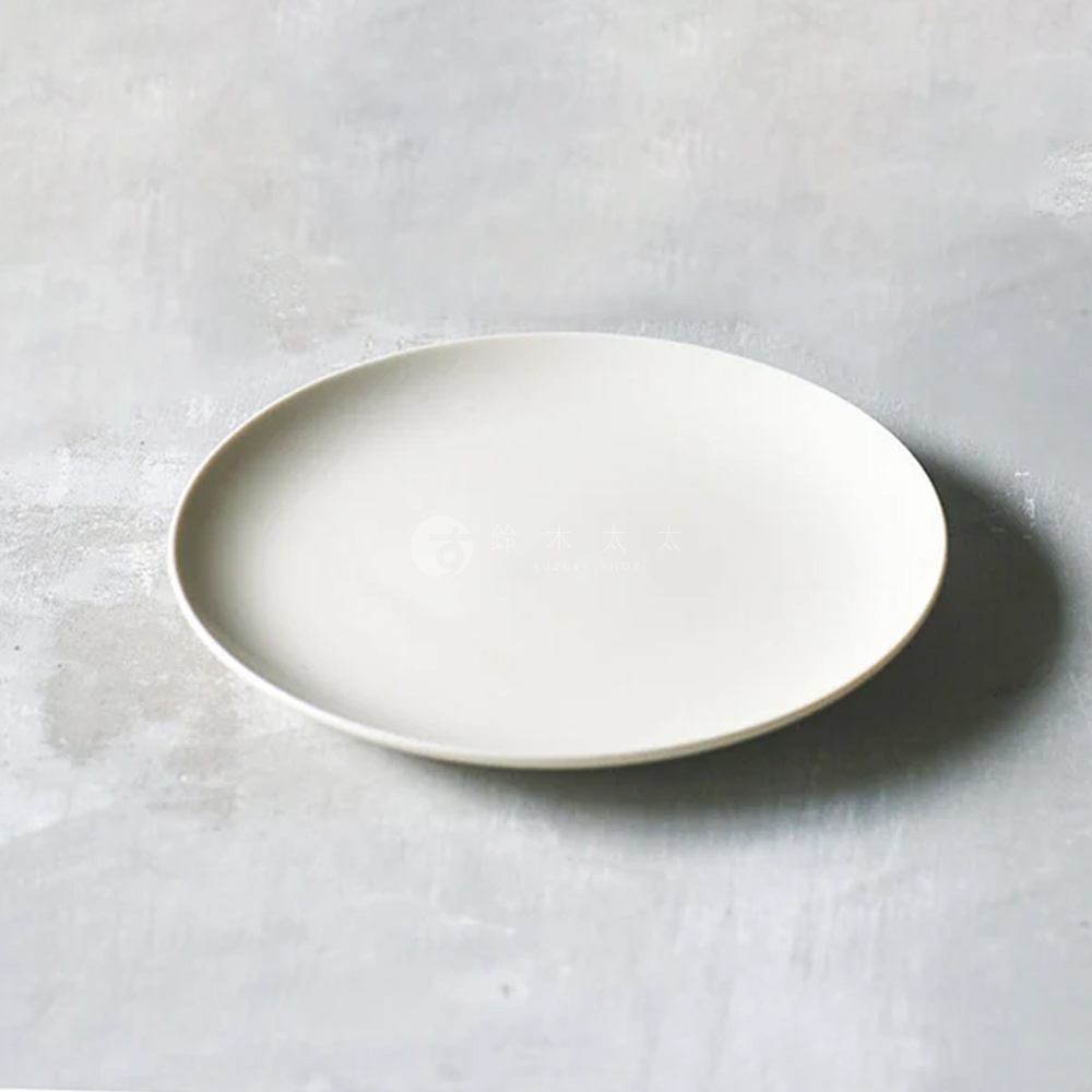 CouLeur 美濃燒簡約素雅質感圓餐盤 M，米白色陶瓷材質，盤面平坦，邊緣帶有微微弧度，置於灰色水泥紋理背景上。