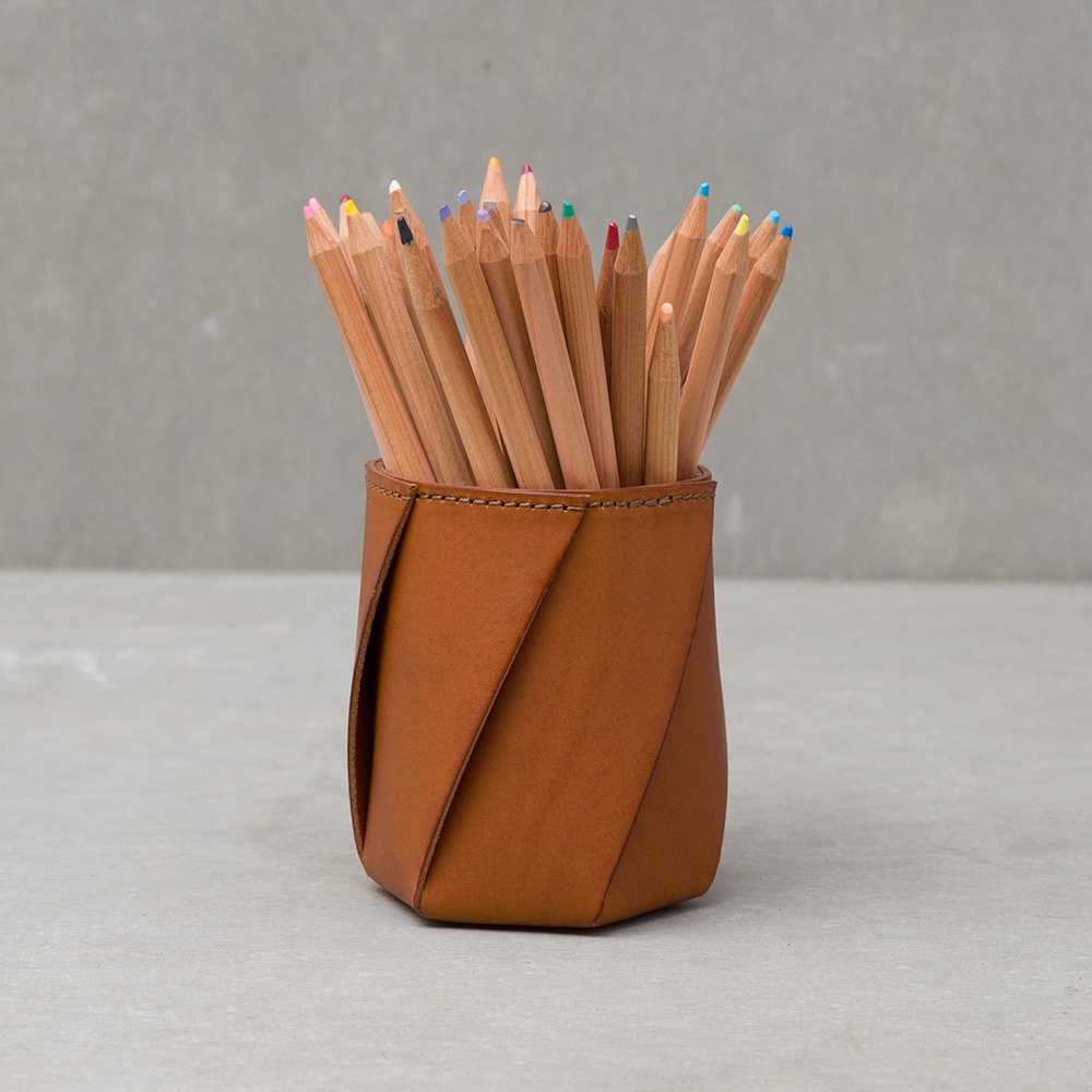 職人手作皮革Organ六角收納筆筒，採用淺棕色皮革製成，筆筒呈現扭轉的六角造型，內部插滿色彩鮮豔的彩色鉛筆。
