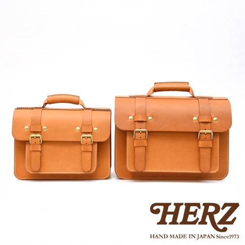 兩只棕褐色皮革製作的雙扣兩用單肩包，一大一小，均有提把、翻蓋和兩個可調節皮帶扣。