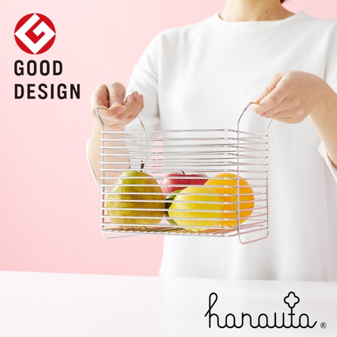 一只手提著一個不鏽鋼深型收納籃，籃子裡有綠色的梨子、紅色的蘋果、黃色的檸檬和橘子。