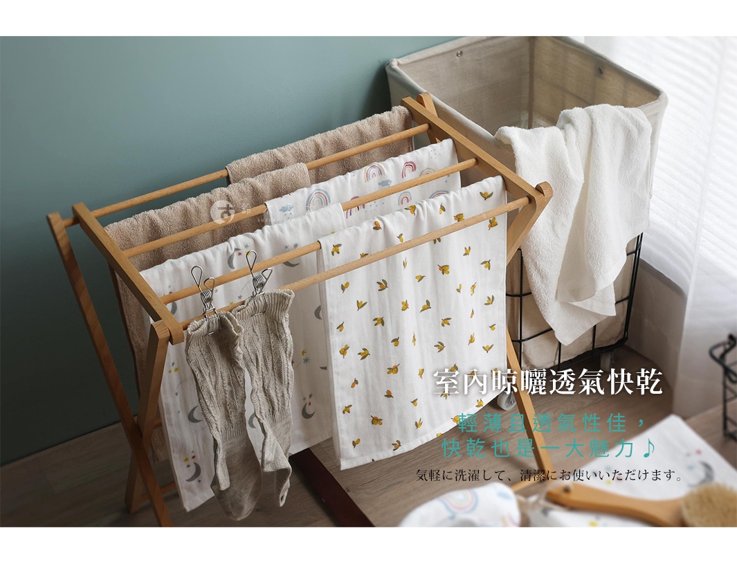 日式簡約木質摺疊曬衣架，掛滿印有可愛圖案的紗布巾，一旁還有竹籃裝著白色毛巾，室內晾曬通風快乾。